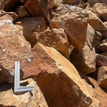 Large reddish-brown rocks with a metal L-shaped tool for scale.