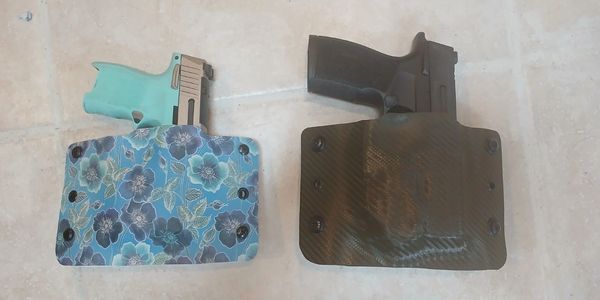 Two handguns in contrasting holsters on a tiled floor.