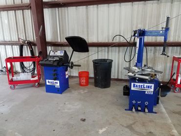 Two blue Baseline tire machines in a garage with red carts and trash bins.