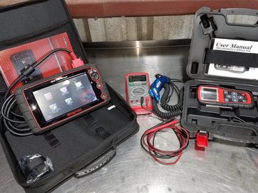 Automotive diagnostic tools including Snap-on devices and a user manual on a metal workbench.