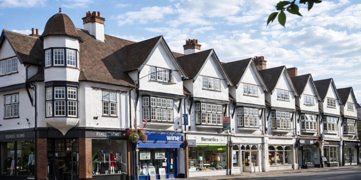 A row of traditional shops with white upper floors and brown roofs under a blue sky.