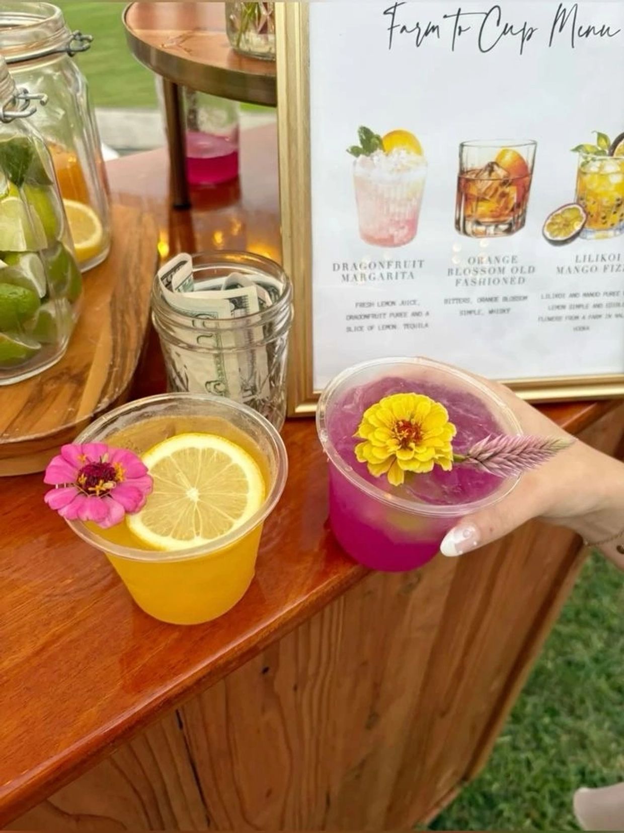 Two vibrant cocktails with floral garnishes on a wooden counter at an outdoor bar.