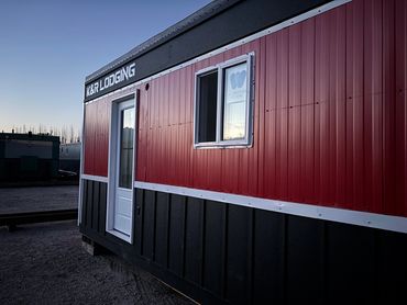 A red and black, all-electric portable lodging unit with a white door and window at dusk. K&R Lodging