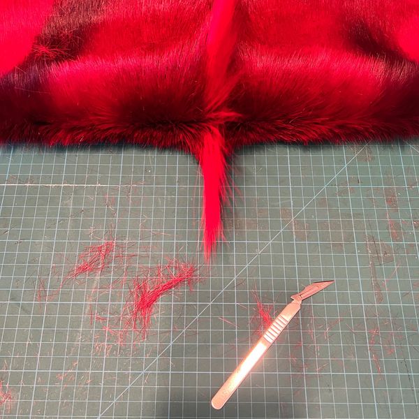 Red fur being trimmed with a scalpel on a cutting mat.
