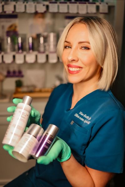 Smiling skincare professional holding beauty products in clinic.