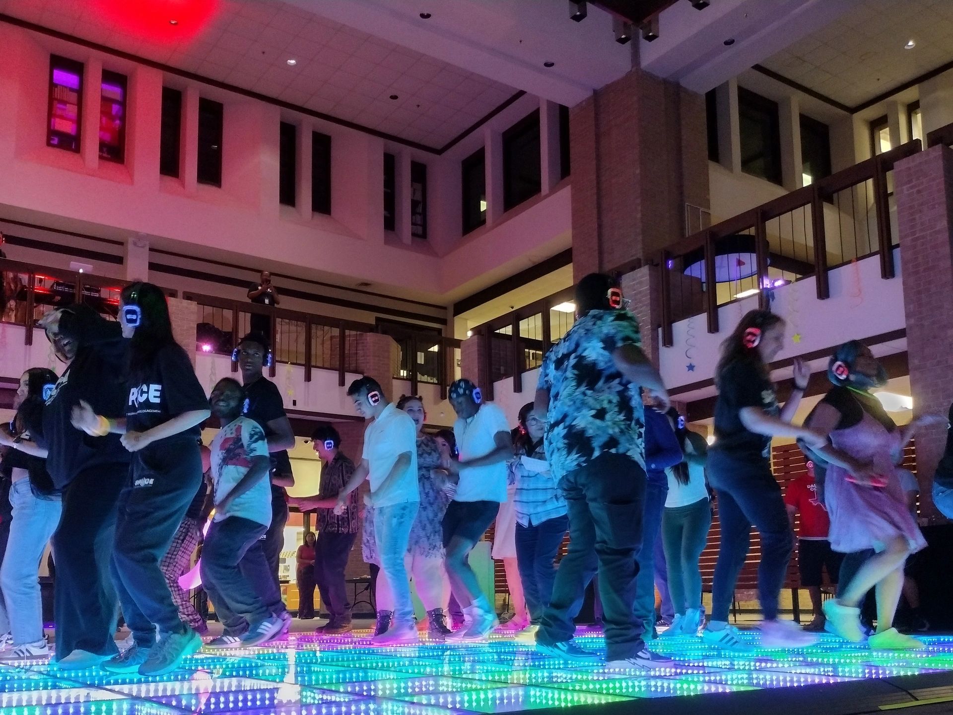 A group of people dancing on a colorful LED floor wearing headphones indoors.