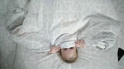 Child peeking out from under a patterned blanket in bed.