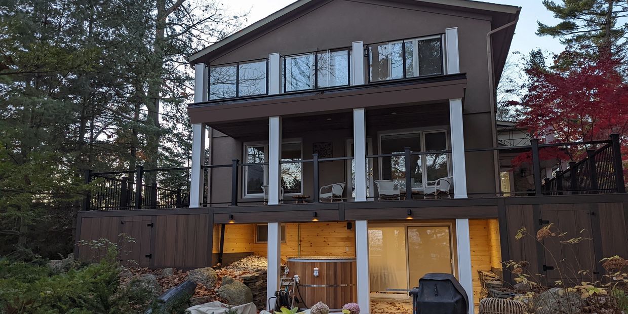 large multi-story brown composite deck wrapping around home with white columns and glass railing