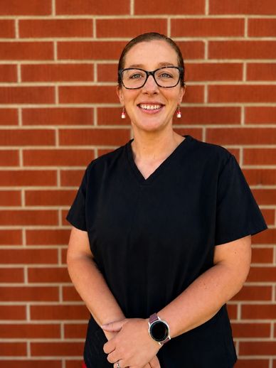 Smiling woman in black scrubs standing against a brick wall.