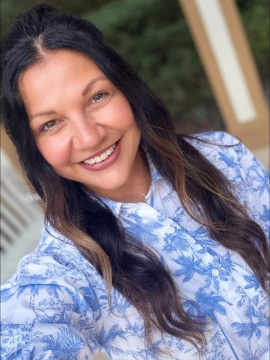 Smiling woman with long hair in a blue and white floral shirt.