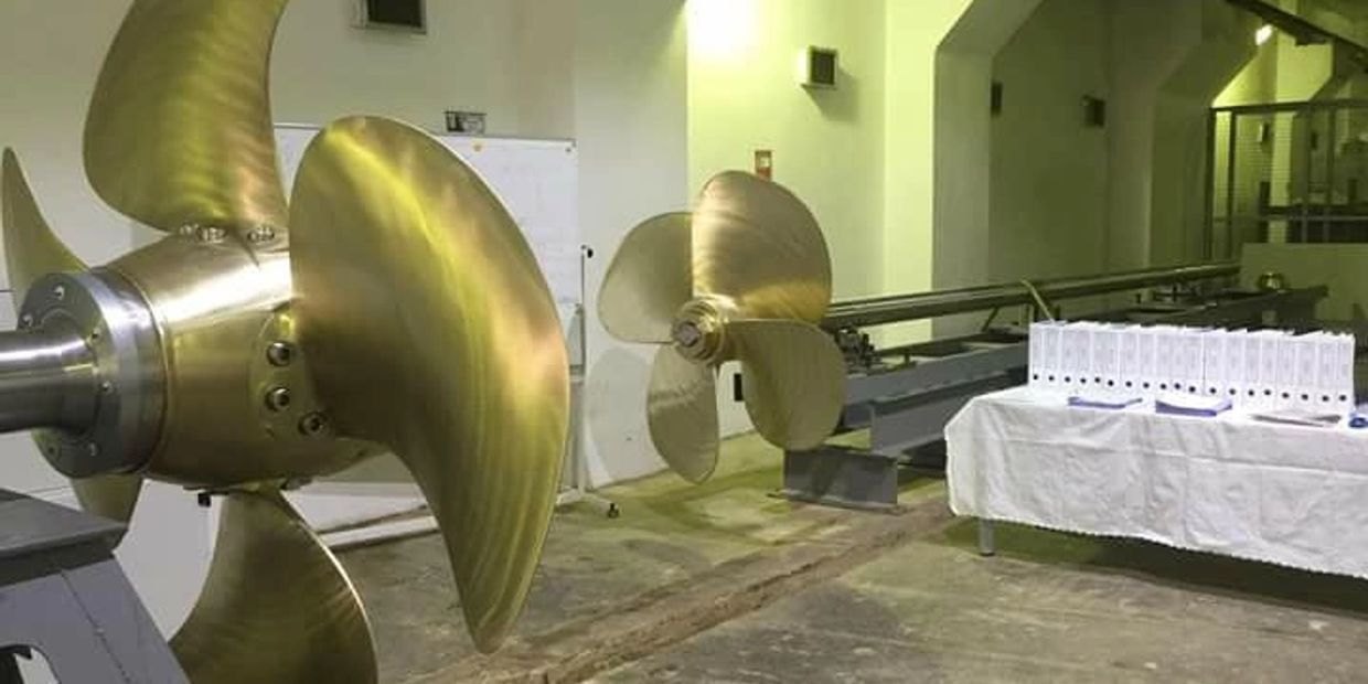 Large brass ship propellers displayed indoors with documents on a table nearby.