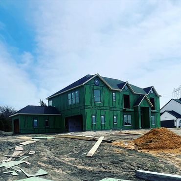 Large two-story house under construction with green sheathing and scattered wood pieces.