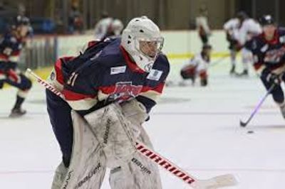 Ice hockey goalie in protective gear ready to defend the goal on the ice rink.