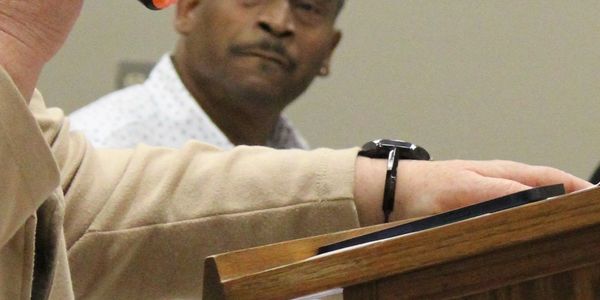 Man attentively listening to a speaker at a podium during an event.