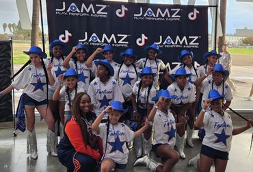 Youth dance team in matching outfits and blue hats posing at JAMZ event.