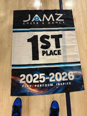 A JAMZ Cheer & Dance 1st place banner for 2025-2026 on a wooden floor.