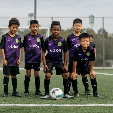 Young soccer players in purple and black uniforms pose on the field with a ball.