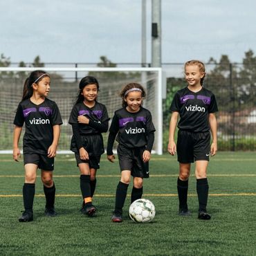 Four young girls in black soccer uniforms walking on a soccer field.