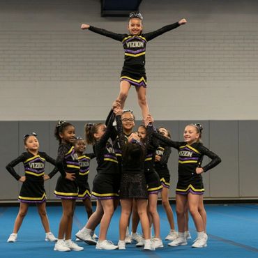 A youth cheerleading team performs a pyramid stunt indoors.