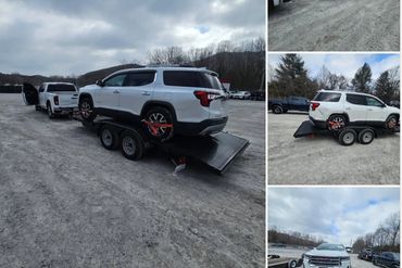 White SUV secured on a trailer hitched to a pickup truck in a gravel lot.