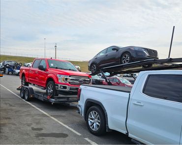 Two pickup trucks transporting vehicles on trailers in a parking lot.