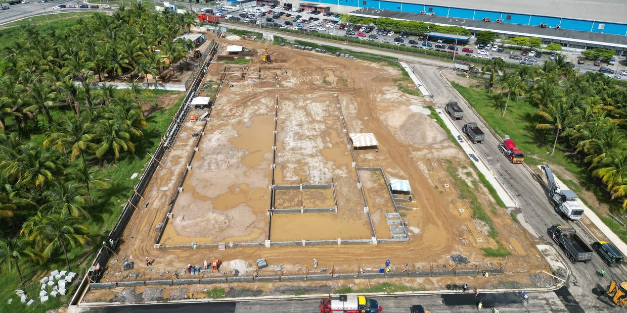 Aerial view of a construction site with machinery and workers near a palm tree grove.