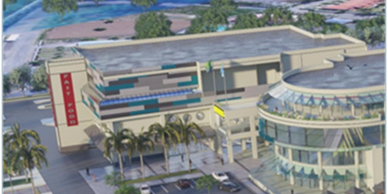 Aerial view of a modern building complex with palm trees and parking spaces.
