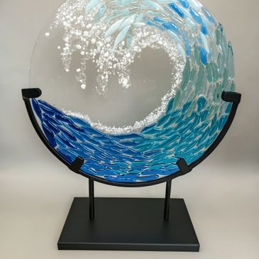 Artistic glass sculpture of a swirling ocean wave in blue and white.