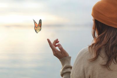 Person releasing a butterfly near a calm lake at sunset.