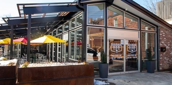 Modern restaurant entrance with glass walls and colorful outdoor umbrellas.