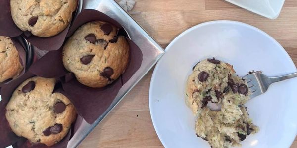 Chocolate chip muffins on a tray and a partially eaten muffin on a plate.