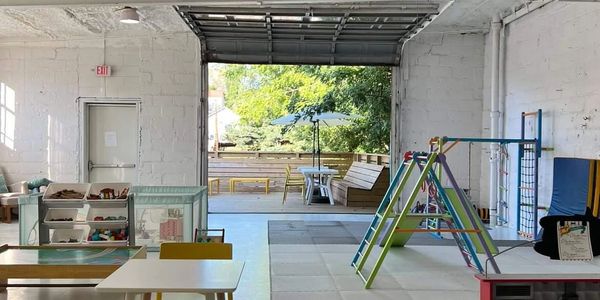 Bright indoor play area with colorful climbing frame and open garage door to outdoor seating.