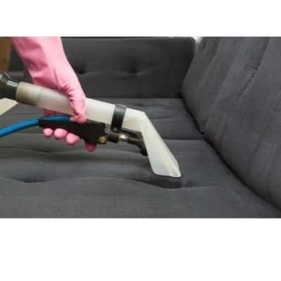 Person cleaning a gray sofa with a steam cleaner wearing a pink glove.