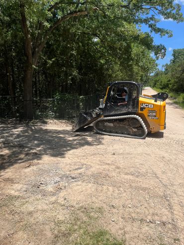 A yellow JCB compact track loader parked on a dirt road near trees.