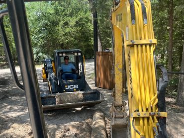 Two construction vehicles working on a dirt path surrounded by trees.