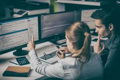 Two programmers analyzing code on dual monitors.