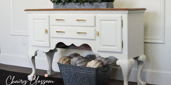 White vintage-style sideboard with a wooden top and a basket of wool underneath.