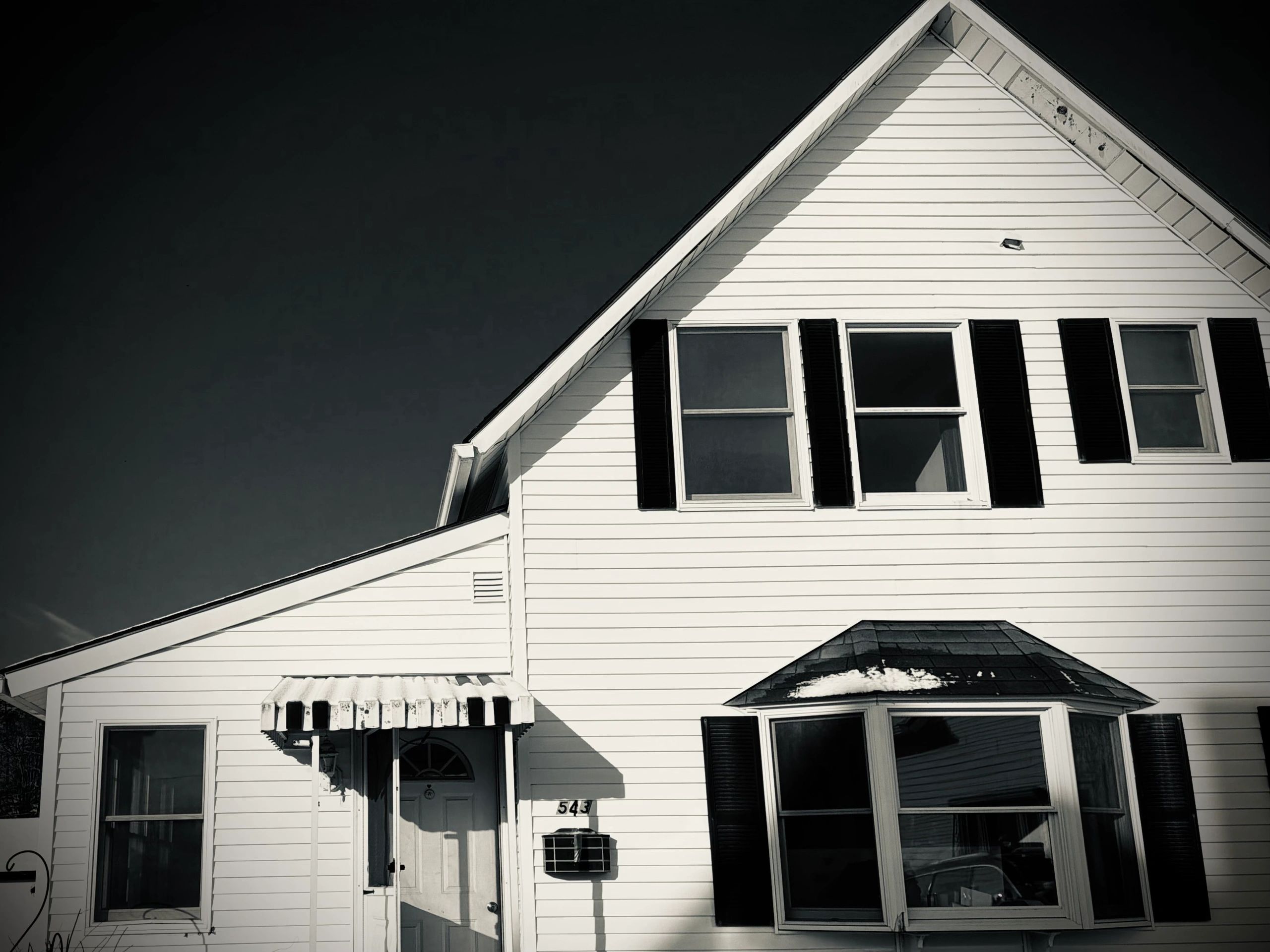 Black and white photo of a house with white siding and dark shutters.