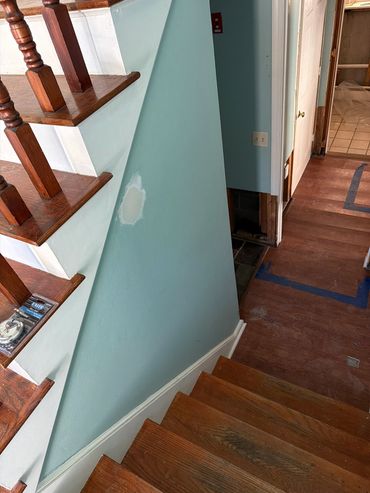 Wooden staircase with blue walls and a patch repair on the wall.
