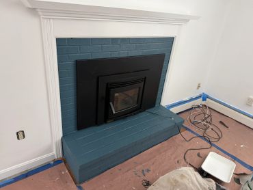 Freshly painted blue brick fireplace with black insert in a room under renovation.