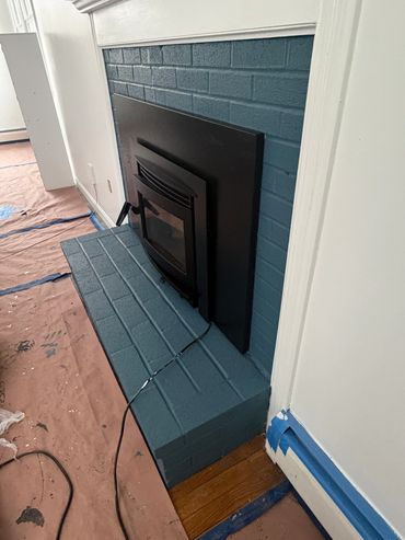 A painted brick fireplace with a wood stove insert and protective floor covering.