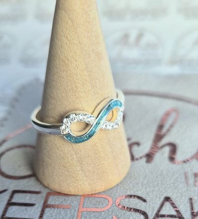 Silver infinity ring with blue accents displayed on a wooden stand.