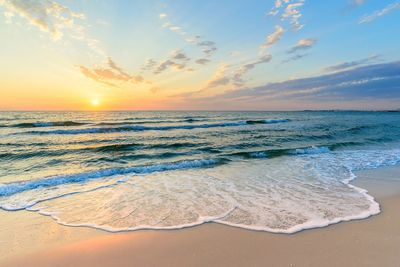 Sunset over a calm beach with gentle waves.