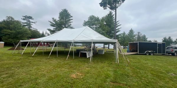 Large white event tent set up on a grassy field near trees and a trailer.