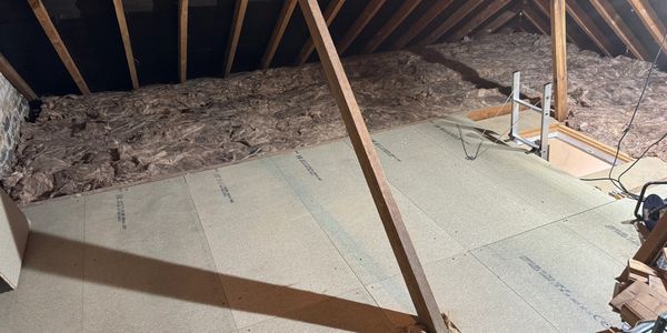 Insulated attic with wooden support beams and plywood floor.
