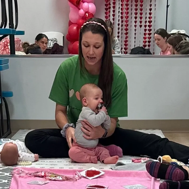 Woman in green shirt interacts with baby sitting on the floor.