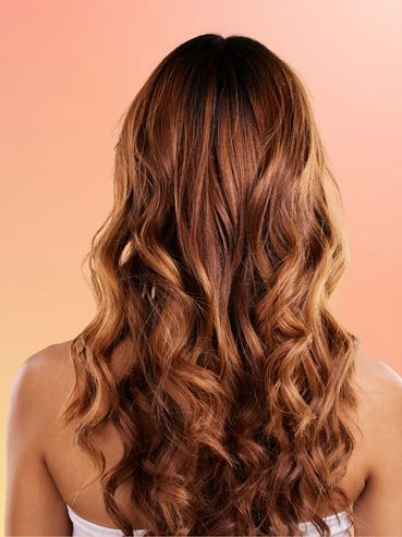 Long, wavy brown hair cascading down a woman's back against a warm gradient background hair blowouts