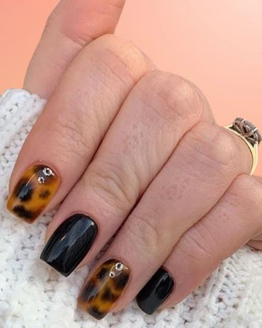 Elegant nails with black polish and leopard print accented with rhinestones.