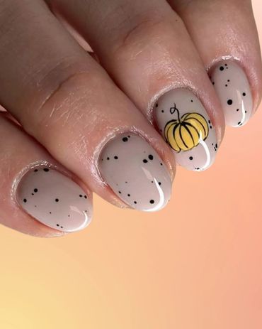 Neutral nails with black speckles and a small yellow pumpkin design.