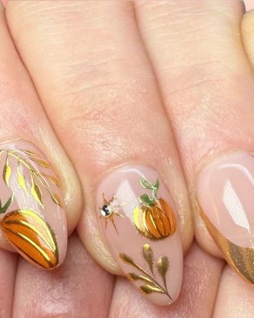 Autumn-themed nail art with pumpkins and gold accents on nude polish.